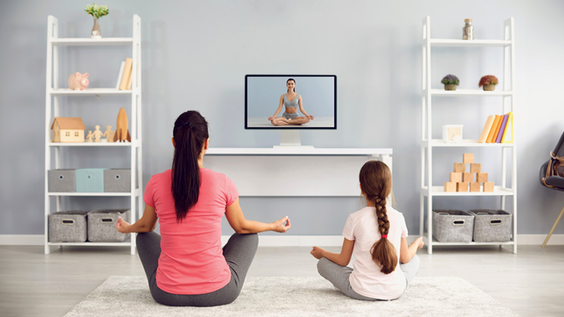 donna e bimba di spalle che fanno yoga davanti alla tv